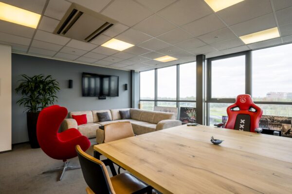 Moderne kantoorruimte aan de Anthony Fokkerweg met een loungehoek, grote ramen, vergadertafel en een opvallende rode gamestoel met Ajax-logo.